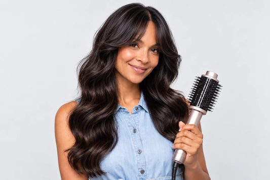 Smiling woman with styled curtain bangs and wavy hair holding a TYMO blowout brush, against a white background.